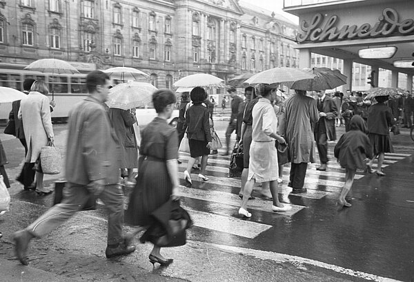 Passanten beim Überqueren der Karlstraße an einem regnerischen Tag im Mai, im Hintergrund die Hauptpost, 1965